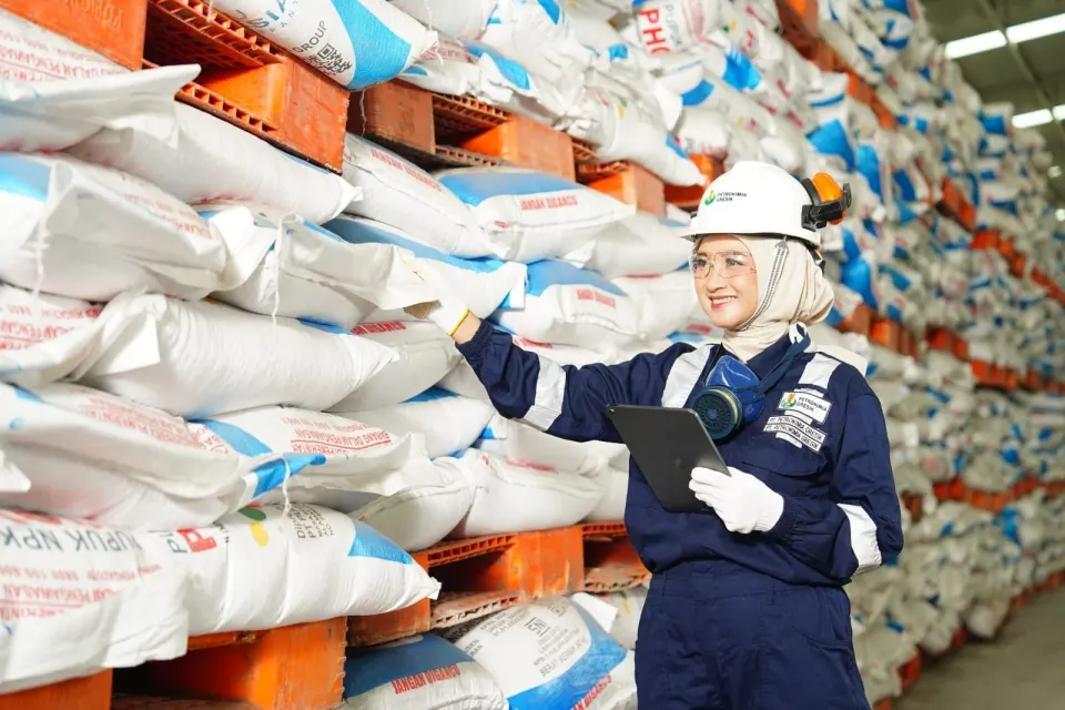 Petugas gudang Petrokimia Gresik memakai helm dan wearpack sambil memeriksa tumpukan karung pupuk